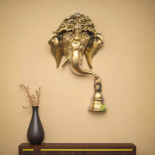 Decorative wall sculpture of an elephant head with a bell on a beige wall.